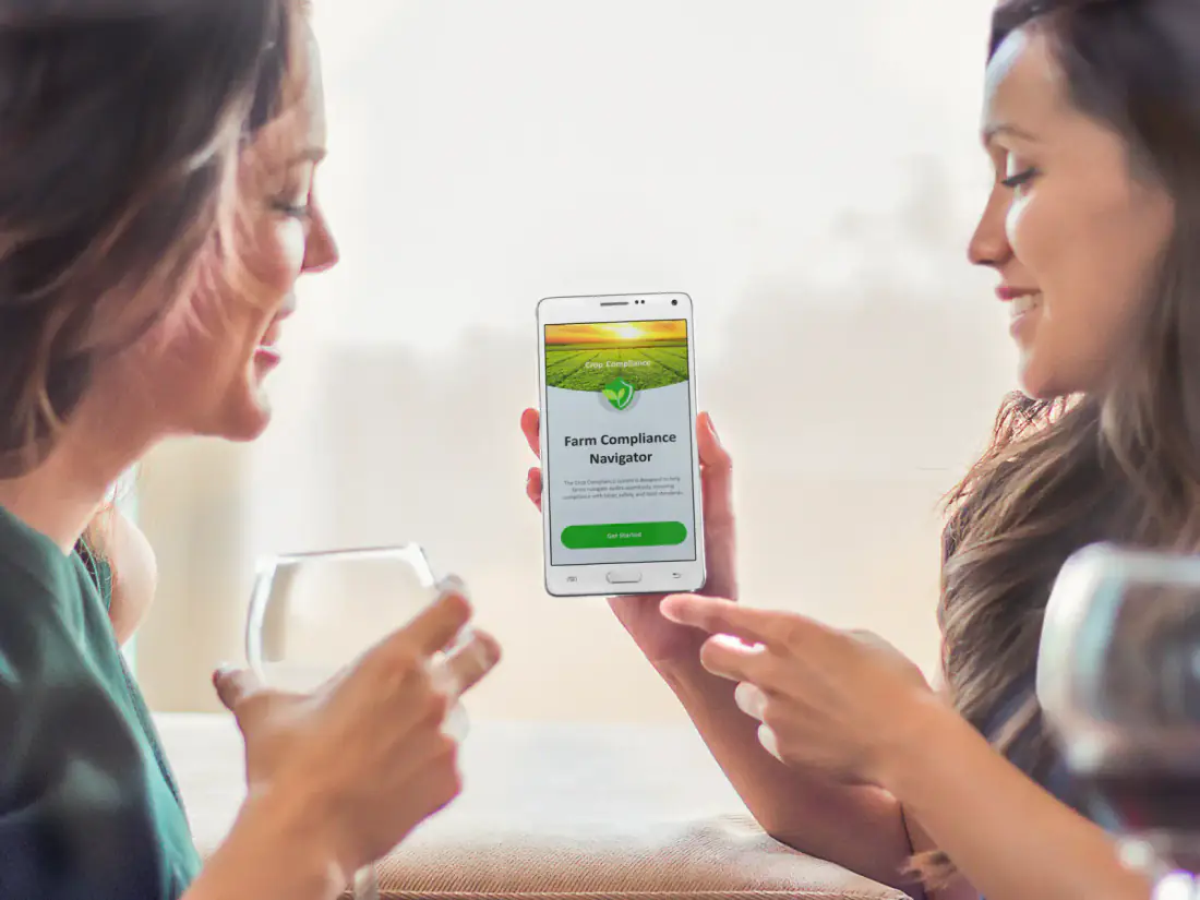 Two people with wine glasses looking at the Crop Compliance app on a phone